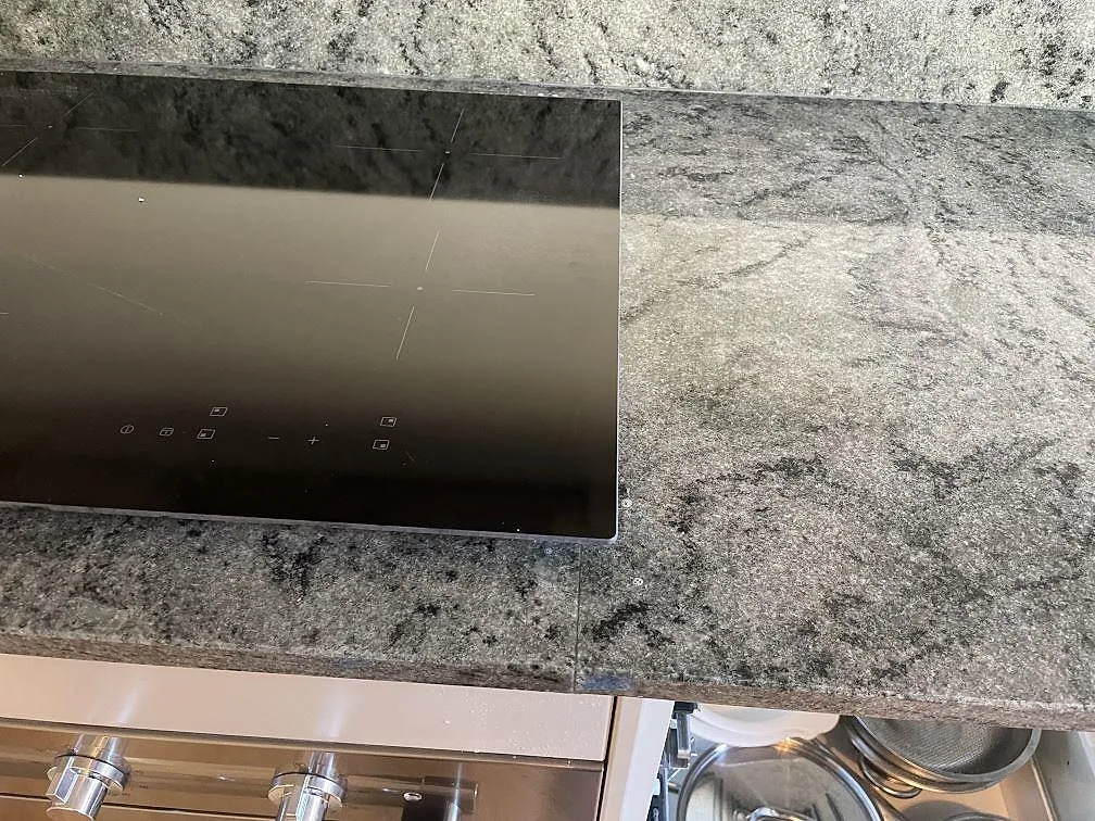 Detalj av svart induktionshäll infälld i polerad Verde Savana granit med tydlig grön och grå ådring i Malmö.