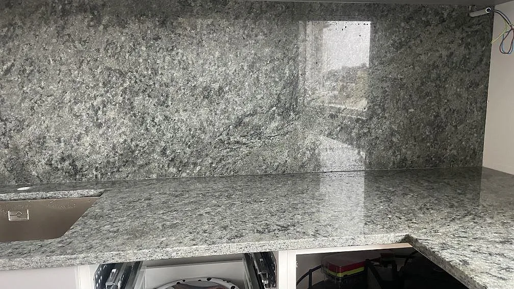 Polerad Verde Savana granit som bänkskiva och stänkvägg runt diskbänken i ett kök under montering i Malmö.