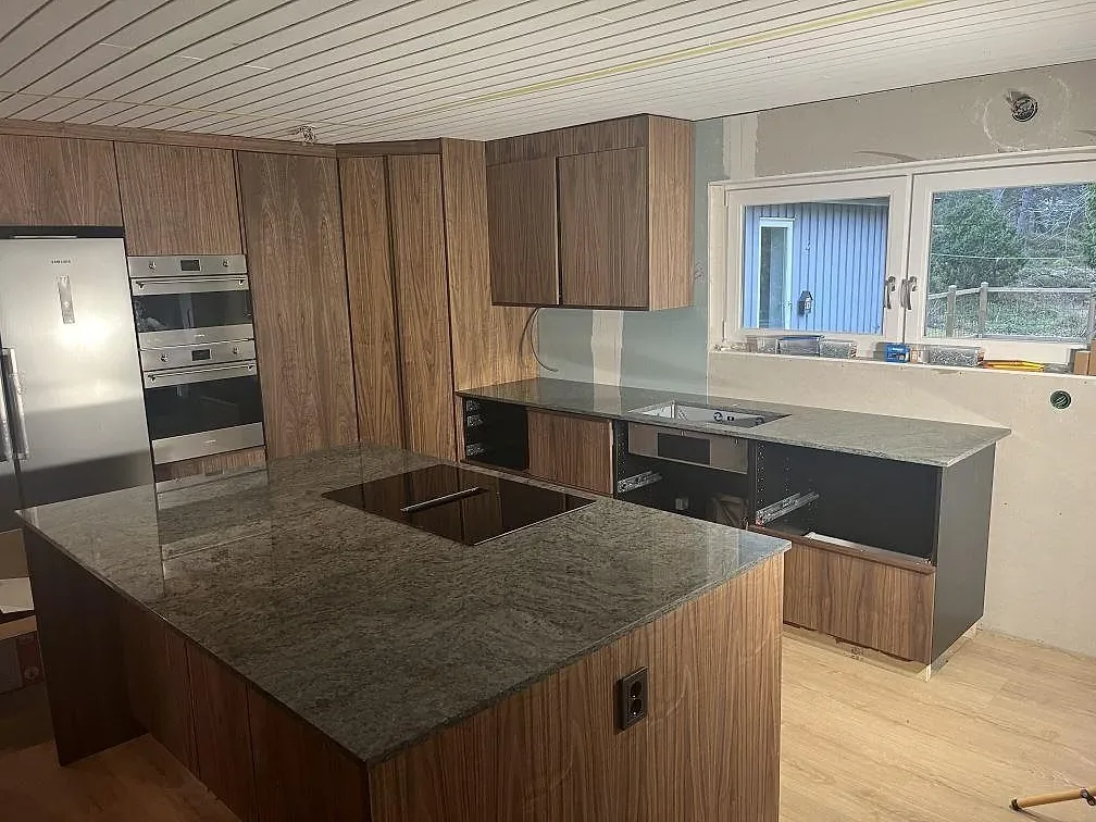 Köksbänkskiva och köksö i polerad Verde Savana granit med träinredning i ett kök i Nyköping.
