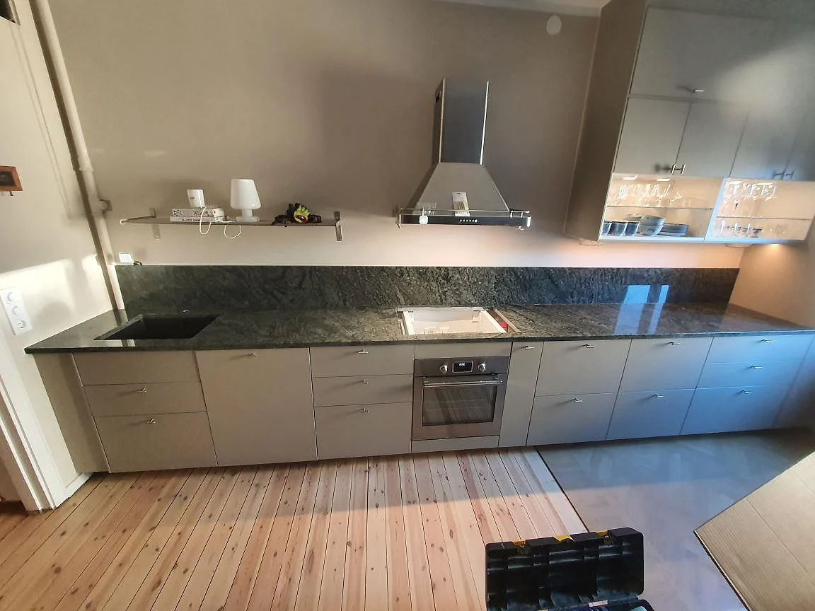 Polerad köksbänkskiva i mörkgrön Verde Savana granit med uppvikt stänkkant i ett kök i Stockholm.
