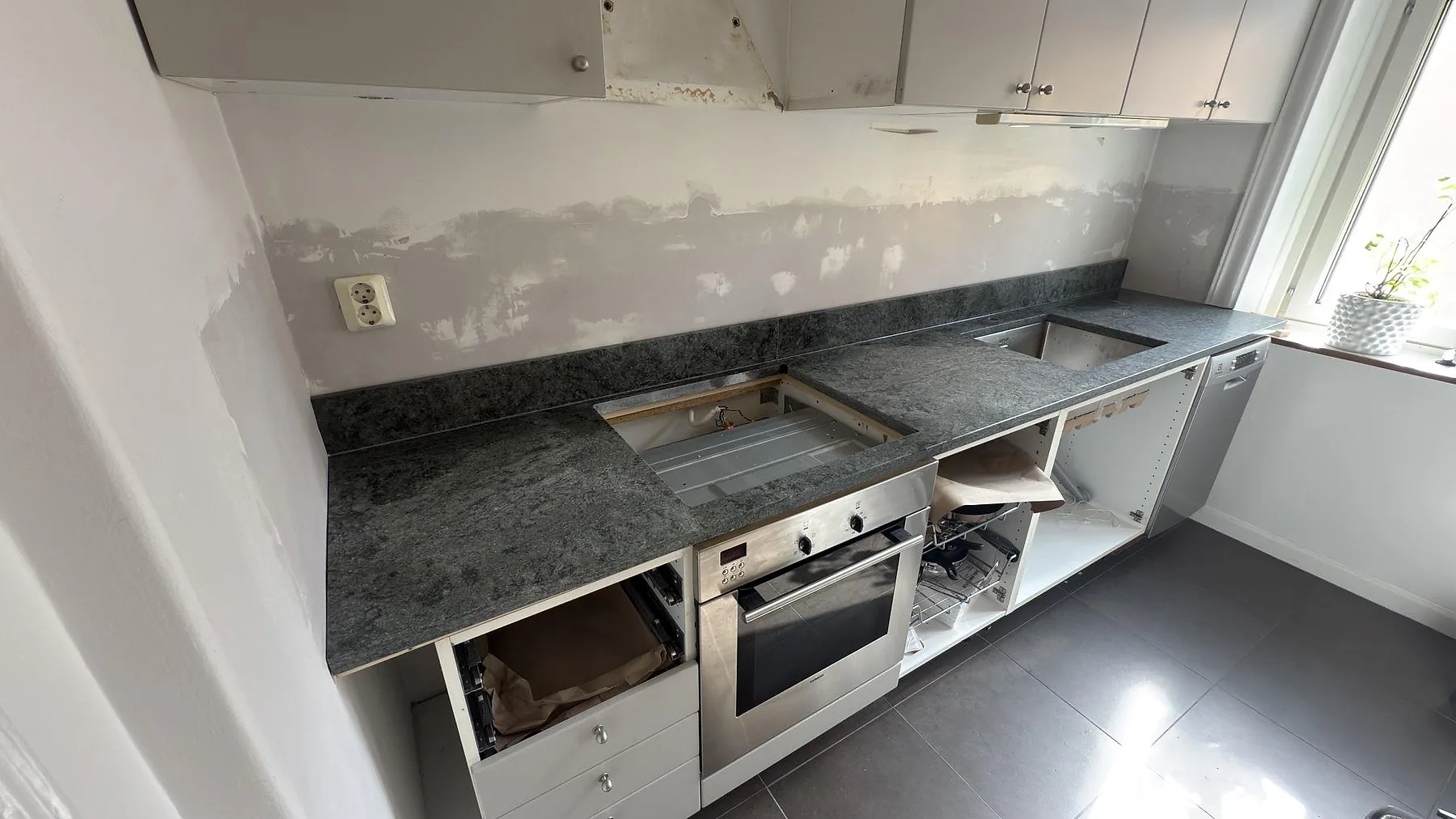 Matt köksbänkskiva i Verde Savana granit med urtag för häll och diskho under montering i ett kök i Stockholm.