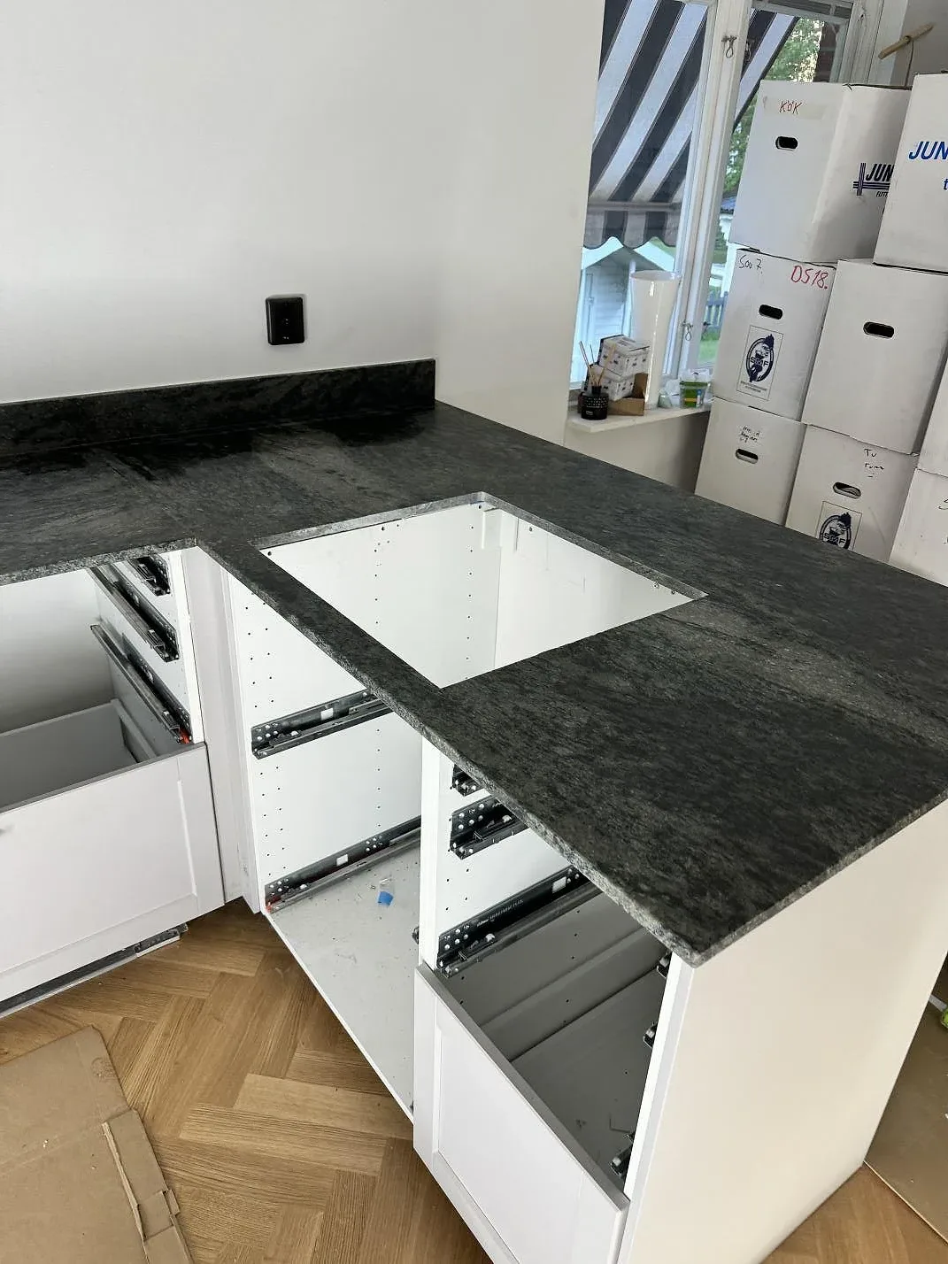 Köksbänkskiva i matt Verde Savana granit med hällöppning, vita köksstommar och fönster i Vaggeryd.