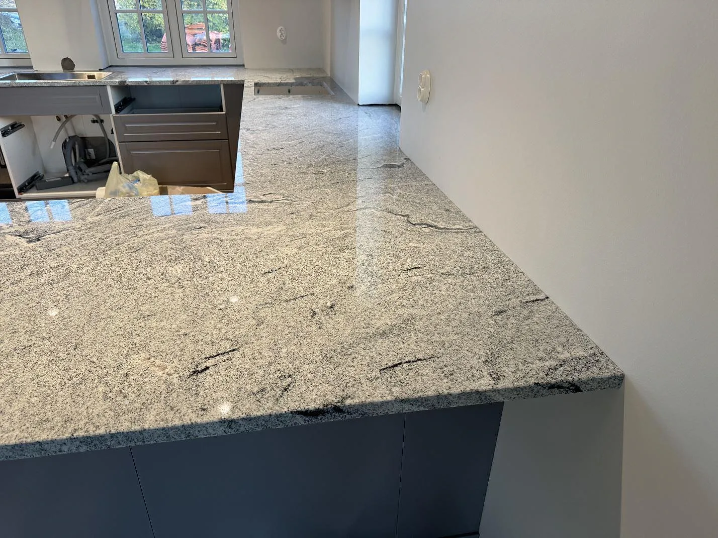 Närbild av polerad köksbänkskiva i Viscont White granit med grå ådring längs väggen i Broddetorp.