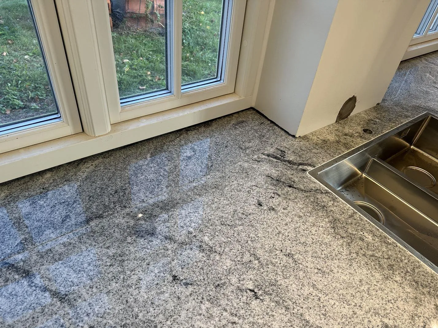 Polerad bänkskiva i Viscont White granit vid fönster och rostfri diskho i ett kök i Broddetorp.