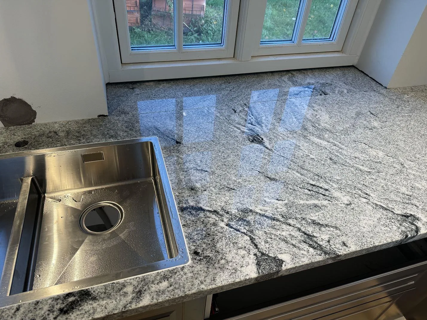 Köksbänkskiva i Viscont White granit, polerad, med rostfri diskho och tydlig mörk ådring i Broddetorp.