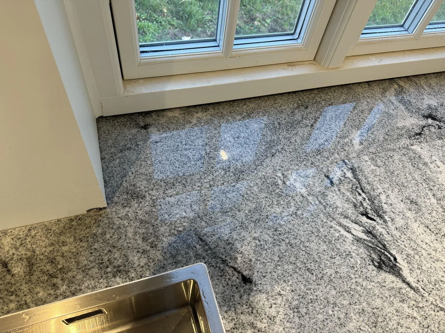 Närbild av polerad Viscont White granit med mörk ådring vid diskbänk och fönster i Broddetorp.