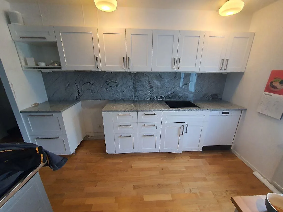 Köksbänkskiva i grå och vit Viscont White granit, polerad, med heltäckande stänkskydd i samma sten och mörk underlimmad diskho i ett kök i Bromma.