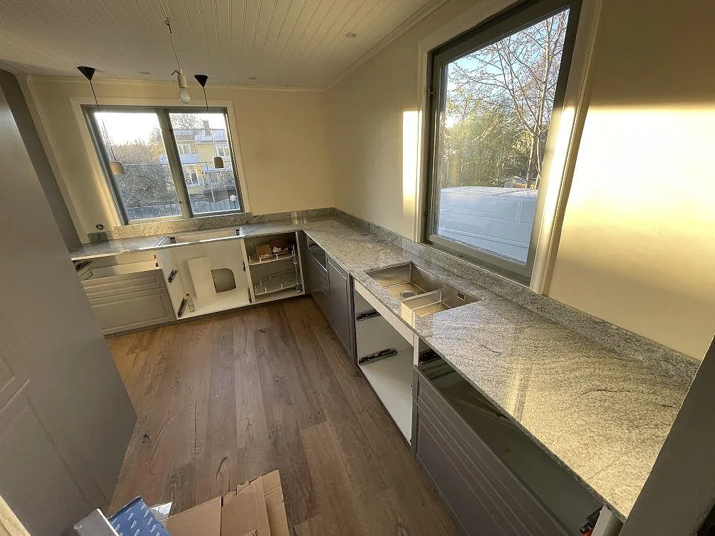 U-formad köksbänkskiva i polerad Viscont White granit, 20 mm, med synliga urtag vid diskplatsen och stora fönster i ett kök under montering i Bromma.