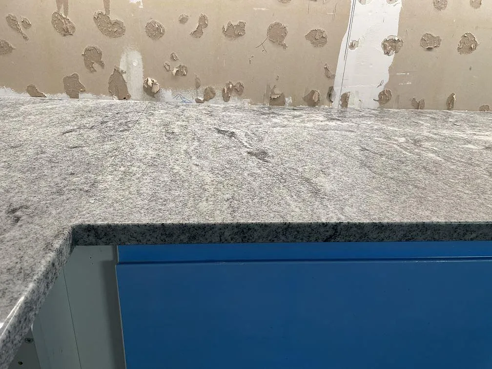 Köksbänkskiva i Viscont White granit, polerad, med flödande grå ådring monterad mot vägg i ett kök under montering i Eslöv.