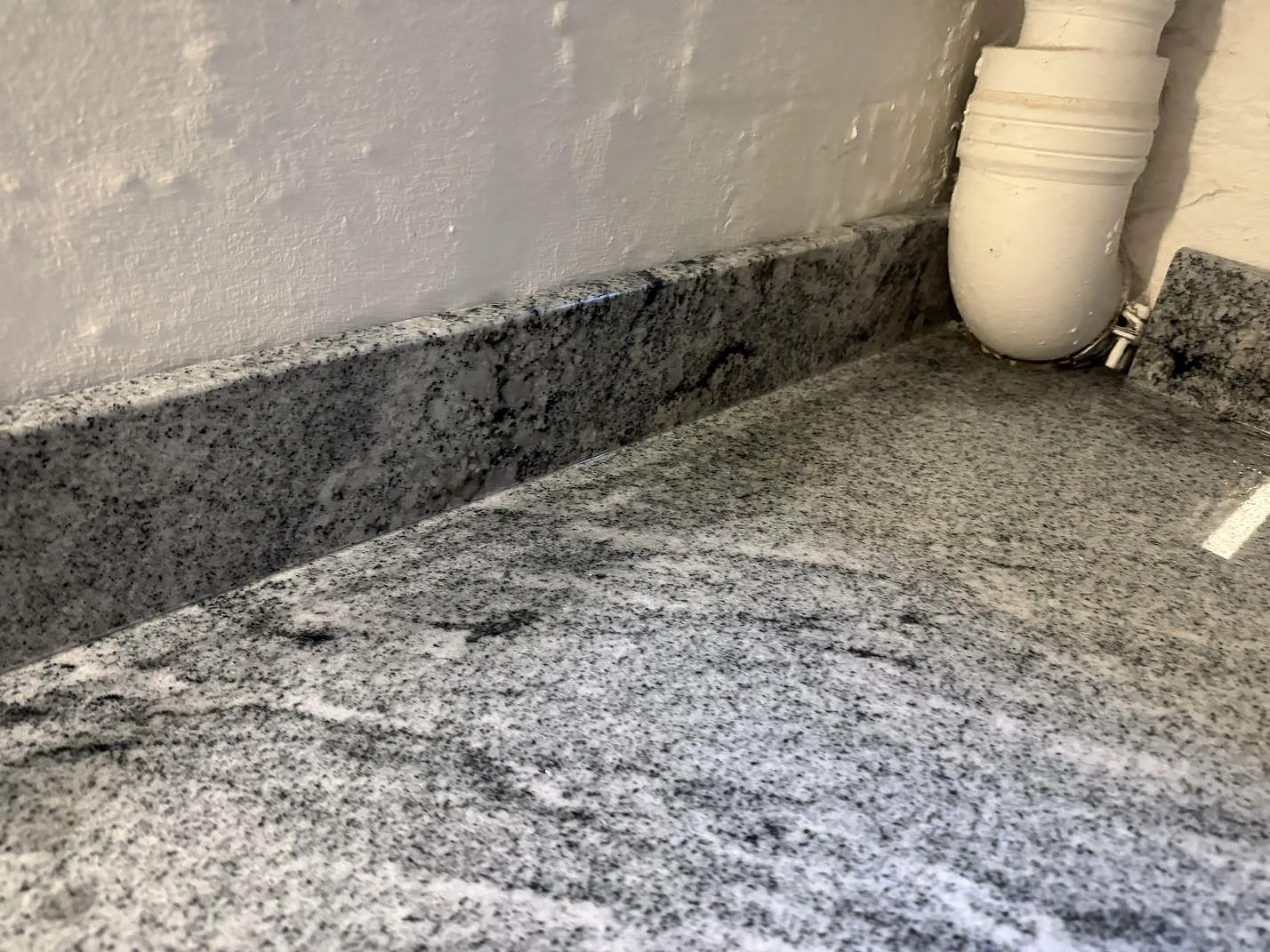 Detaljbild av den polerade ytan och stänklisten i Viscont White granit i Frederiksberg.