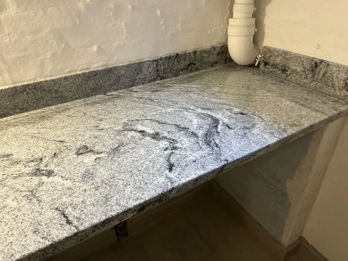 Lång arbetsyta i polerad Viscont White granit med uppvikt stenkant mot putsad vägg i Frederiksberg.