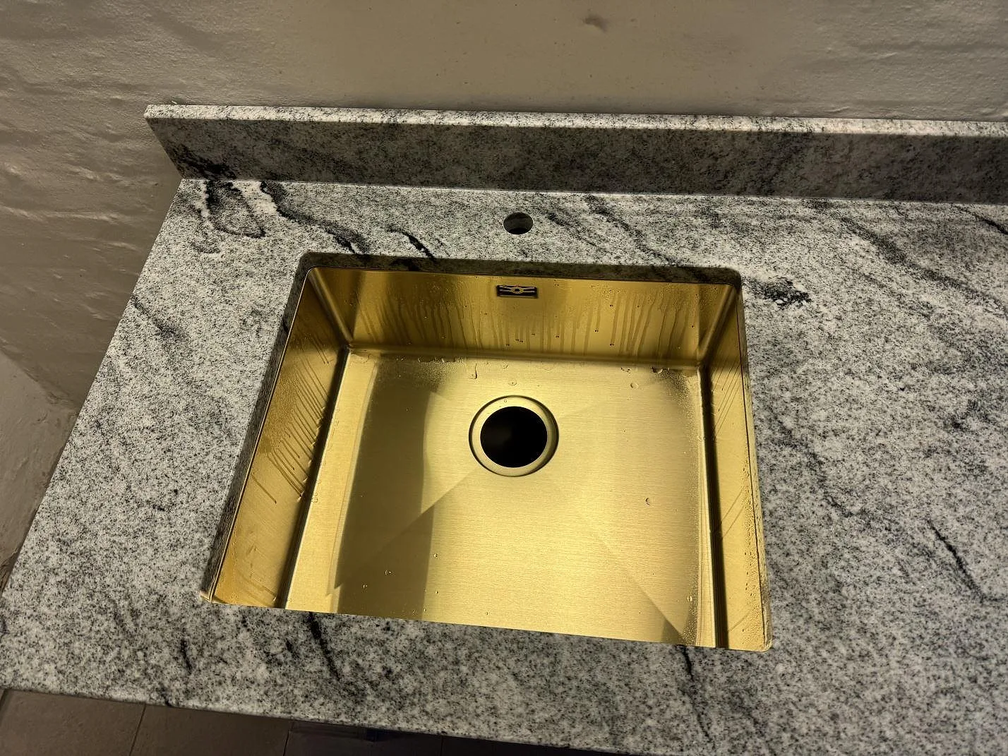 Närbild på mässingsfärgad ho monterad under en polerad bänkskiva i Viscont White granit i Frederiksberg.