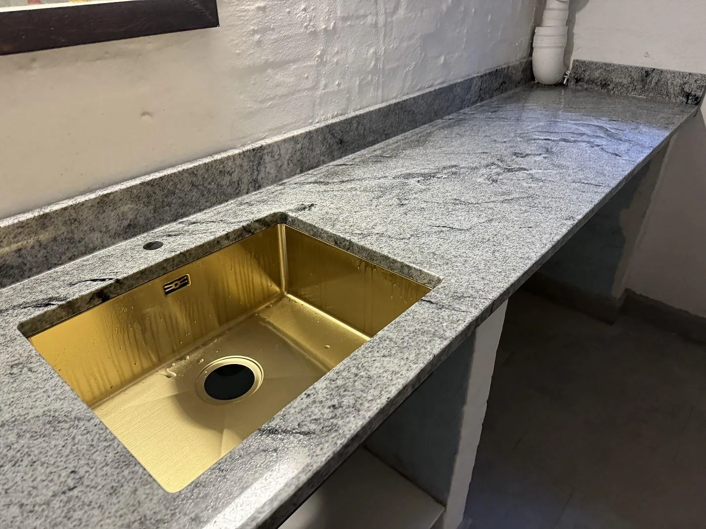 Bänkskiva i polerad Viscont White granit med mässingsfärgad underlimmad ho och uppvikt stenkant i Frederiksberg.