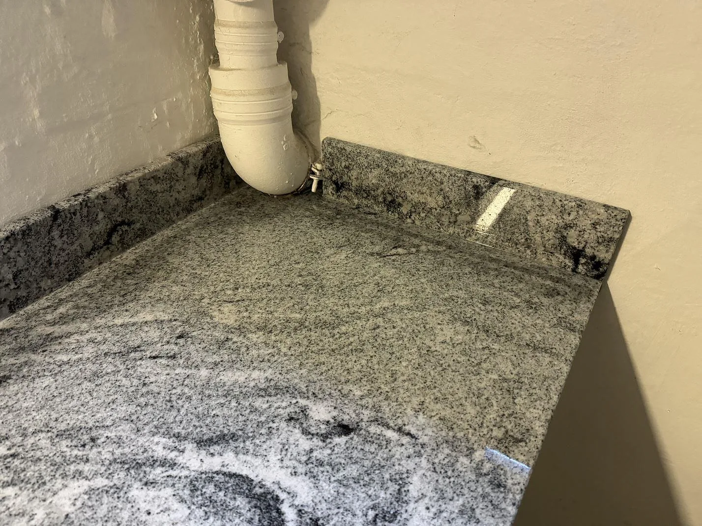 Hörnsektion av polerad Viscont White granit med uppvikt stenkant och synliga vägganslutningar i Frederiksberg.