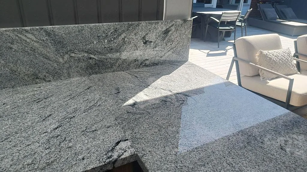 Viscont White granit i polerad yta med uppvikt stänkkant och uteplatsmöbler vid ett utekök i Göteborg.