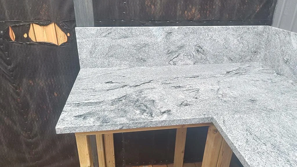 Polerad Viscont White granit som bänkskiva och stänkkant i ett utekök mot mörk trävägg i Göteborg.