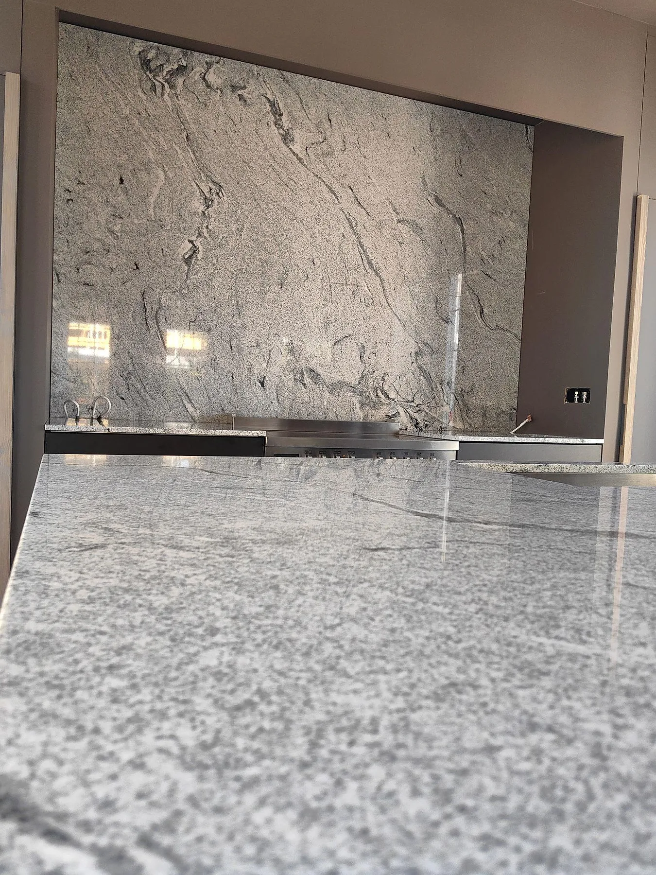 Närbild av polerad Viscont White granit på köksö framför hög stänkvägg i ett kök i Gustavsberg.
