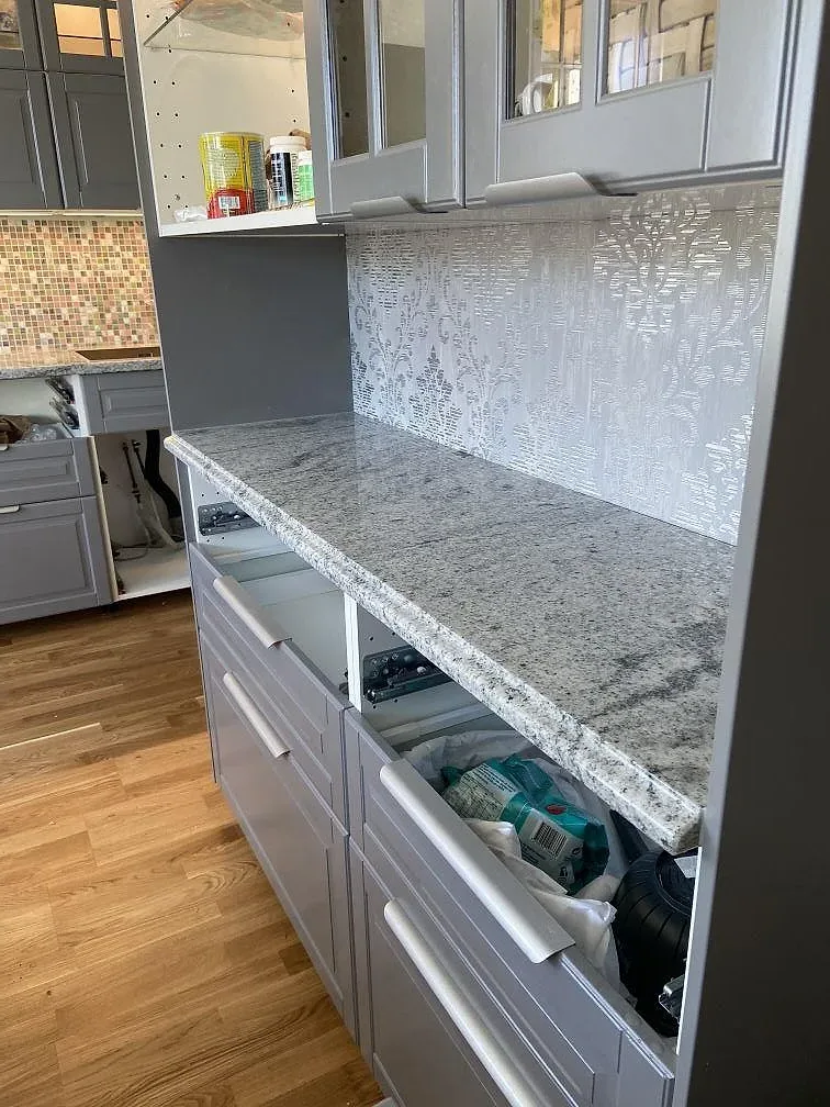 Köksbänkskiva i granit Viscont White, vit med grå ådring, mot grå luckor och ett mönstrat stänkskydd i ett kök i Hisings Kärra, Göteborg.
