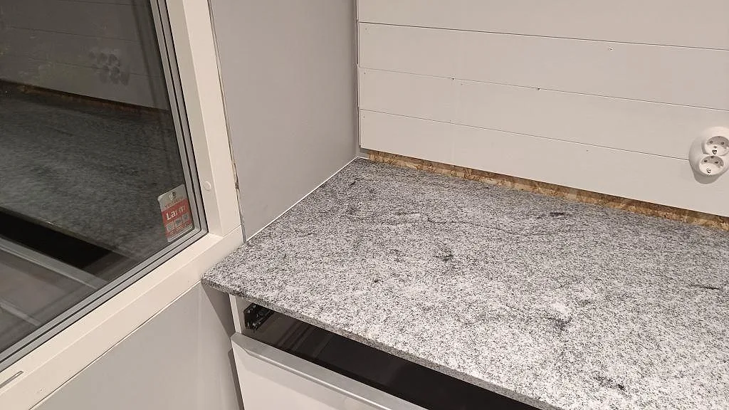 Bänkskiva under fönster i polerad Viscont White granit med ljus väggpanel i ett kök i Höllviken.