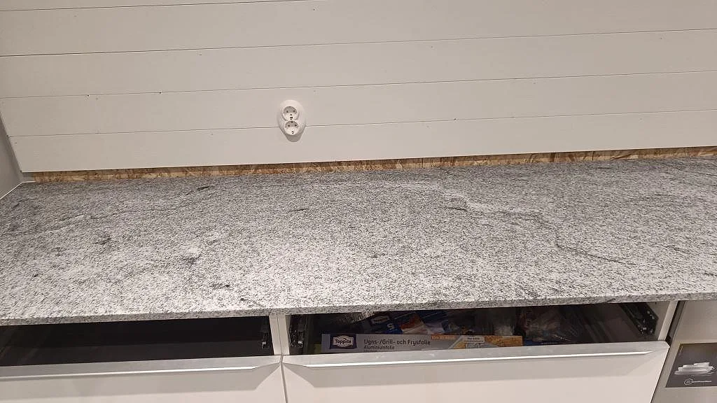 Lång köksbänkskiva i polerad Viscont White granit med uppvikt stenkant över vita stommar i Höllviken.