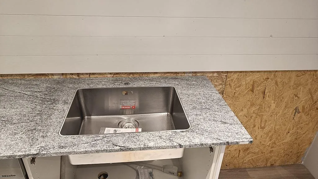 Närbild på underlimmad rostfri diskho i polerad Viscont White granit med grå ådring i Höllviken.