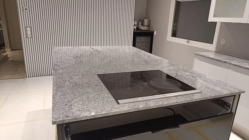 Köksö i polerad Viscont White granit med häll och anslutande väggbänk i ett kök i Höllviken.