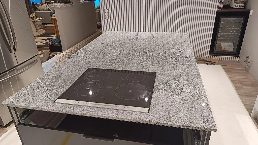 Köksö i polerad Viscont White granit med häll, kyl och väggbänk synliga i köket i Höllviken.