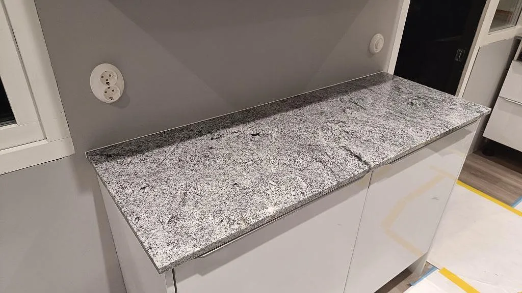 Sidobänk i polerad Viscont White granit vid fönster med grå vägg och låg stenkant i ett kök i Höllviken.
