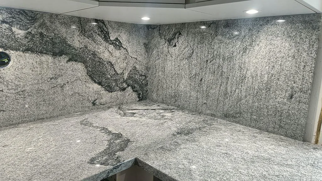 Hörnparti i Viscont White granit med kraftig ådring över bänkskiva och uppvikt stänkskydd i ett kök i Hörby.
