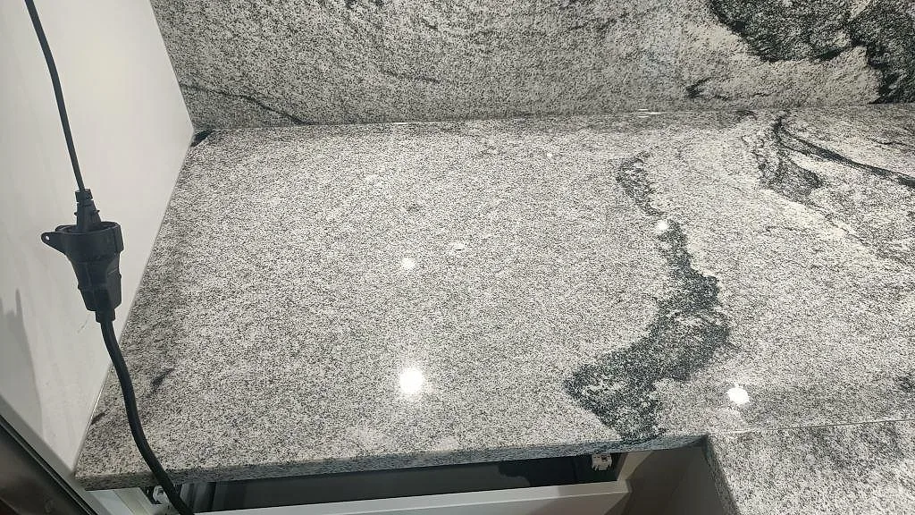 Närbild på den polerade ytan i Viscont White granit som visar grå silkeslen textur och en mörk ådra i ett kök i Hörby.
