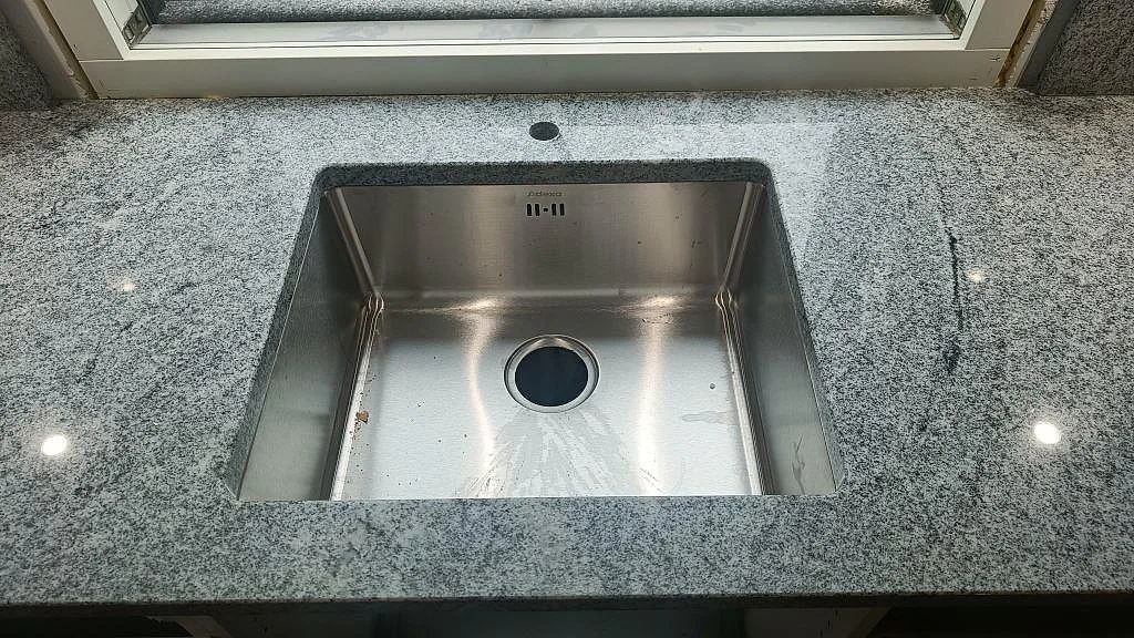 Underlimmad rostfri diskho infälld i polerad Viscont White granit i ett kök i Hörby.