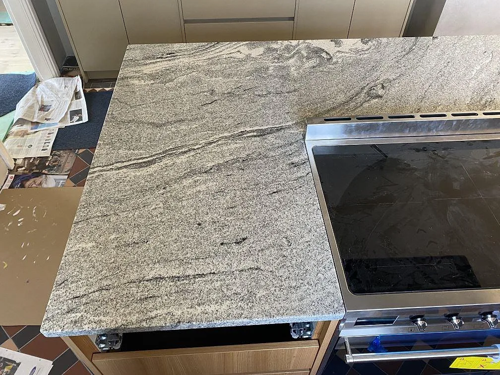 Närbild av polerad Viscont White granit runt spisen, med grå ådring i en köksö under montering i Jämshög.