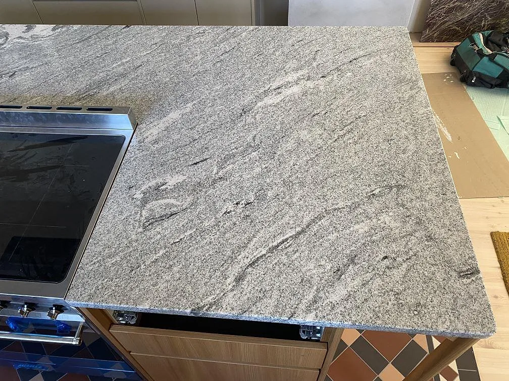 Detalj av Viscont White granit med kraftig grå ådring bredvid spisen på en polerad köksö i Jämshög.