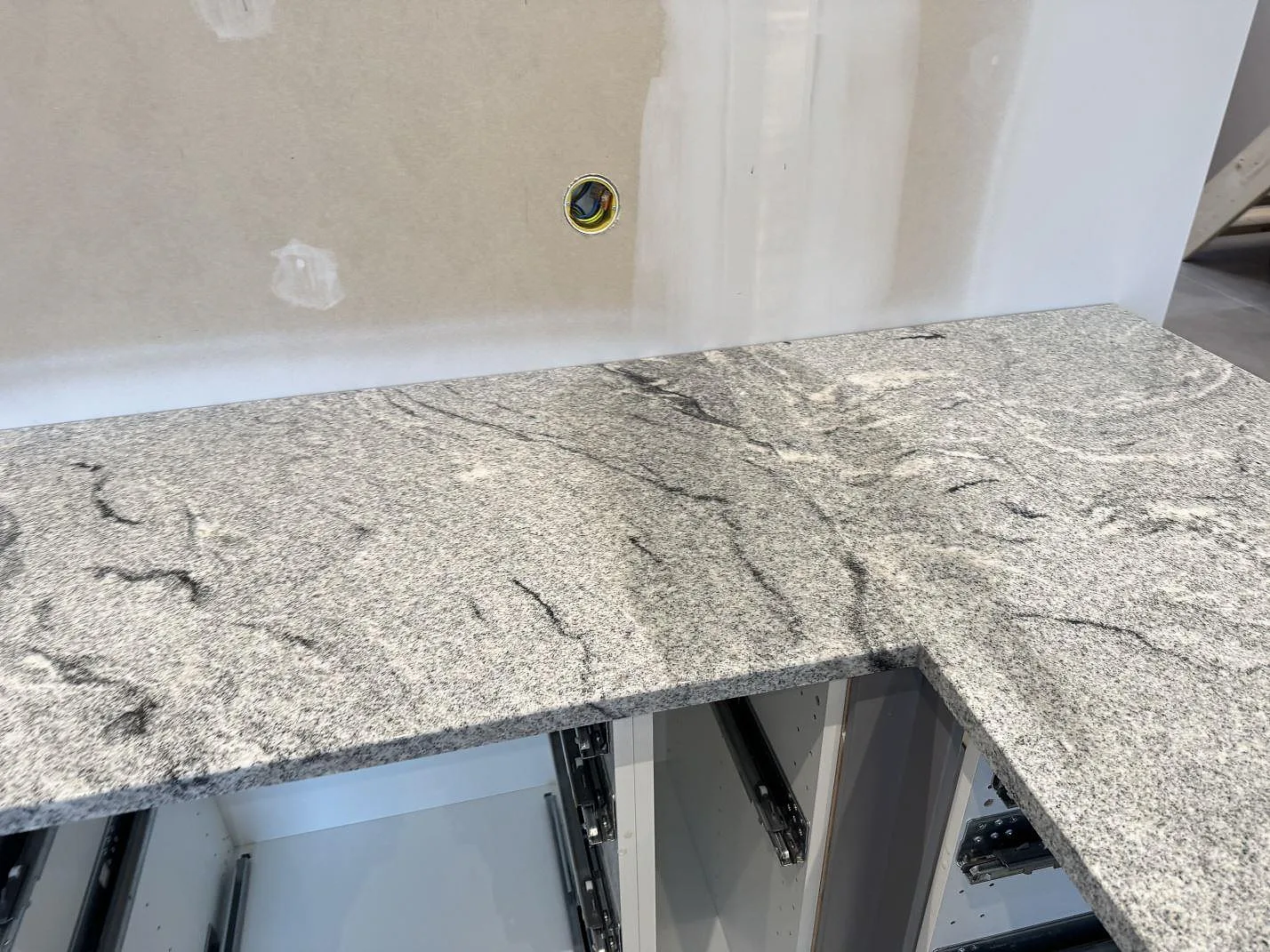 L-formad köksbänkskiva i polerad Viscont White granit med gråsvart ådring mot vägg i Kävlinge.