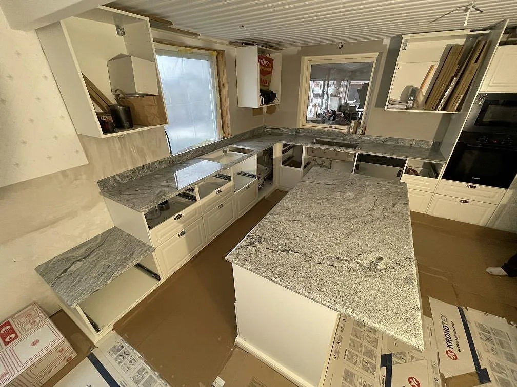 Köksbänkskiva och köksö i ljust grå Viscont White-granit, polerad, med tydlig grå ådring i ett U-format kök i Kumla, fotat under montering.
