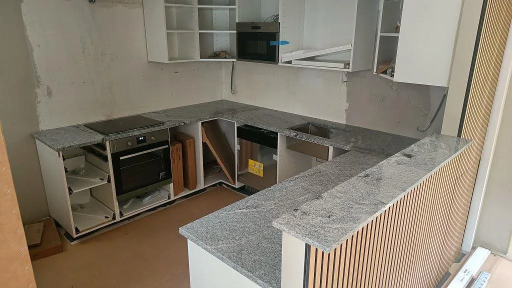 Köksbänkskiva i Viscont White granit, polerad, i ett U-format kök med köksö och barhörna i Lund, fotograferat under montering.