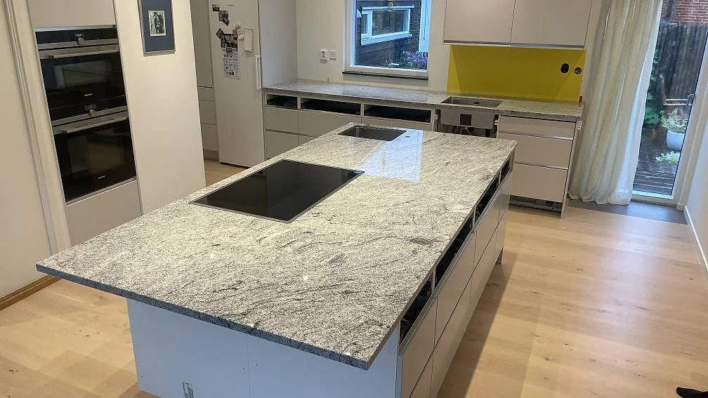 Köksö och bänkskivor i Viscont White granit, 30 mm polerad, med svart häll och ljusgrå ådring i ett kök i Malmö.