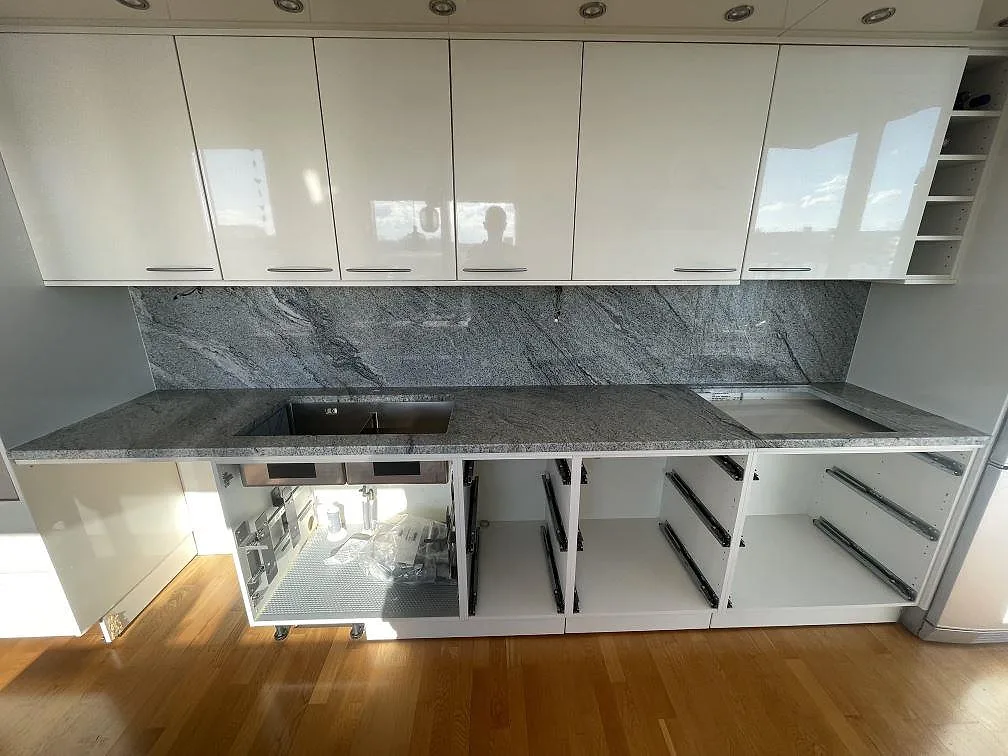 Köksbänkskiva i Viscont White granit, polerad, med heltäckande stänkvägg i samma sten och urtag för underlimmad diskho i ett kök med vita högglansluckor i Malmö.
