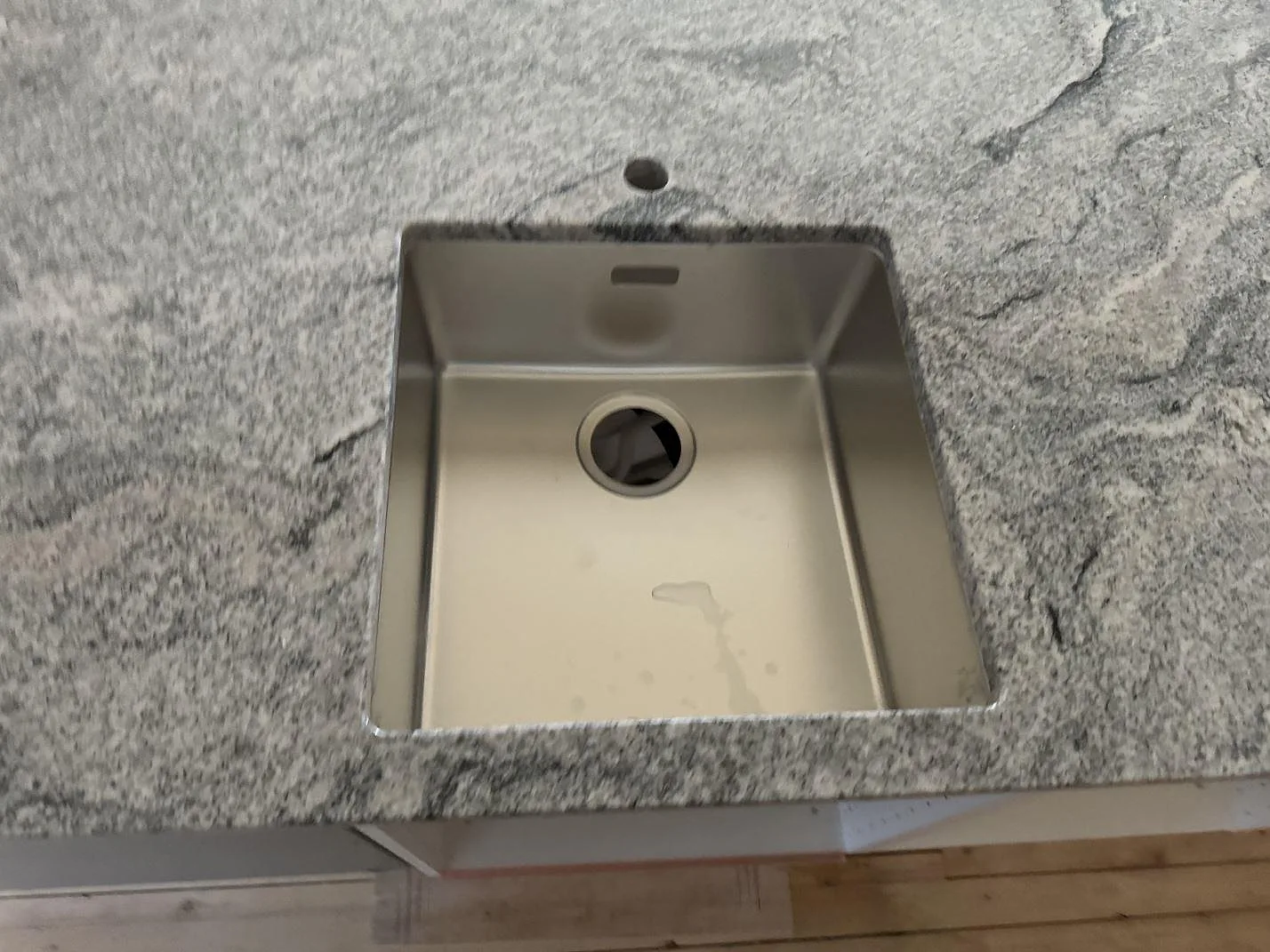 Detaljbild av polerad Viscont White-granit med rostfri diskho och blandarhål i köksbänkskivan i Olofström.
