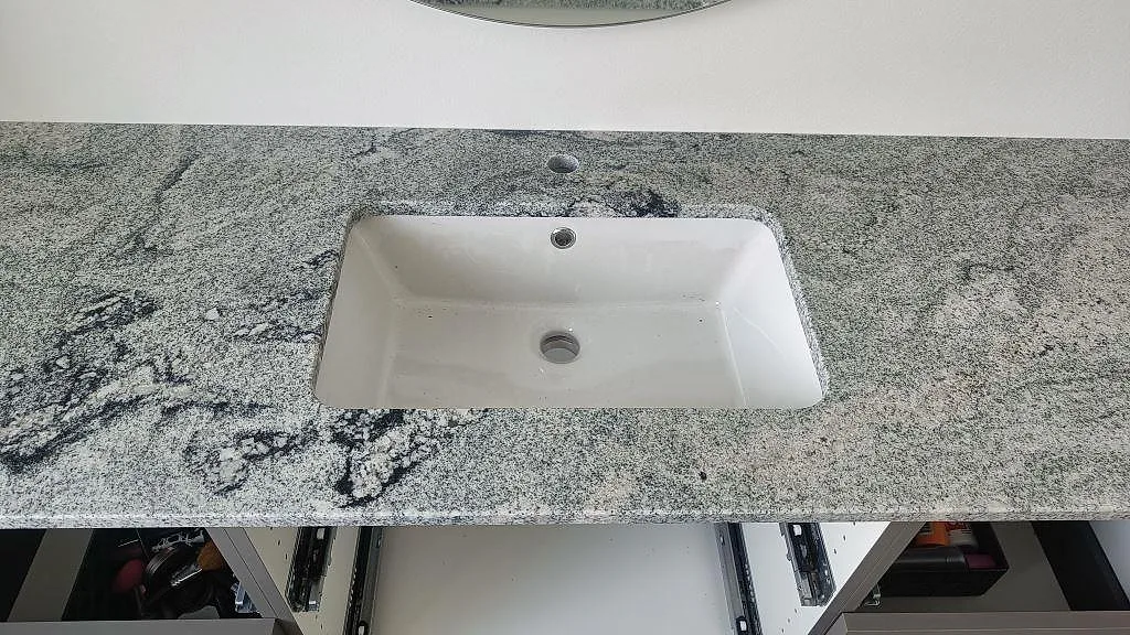 Närbild av badrumsskiva i Viscont White granit med vitt tvättställ under stenen och polerad grå ådring i Ringsted.