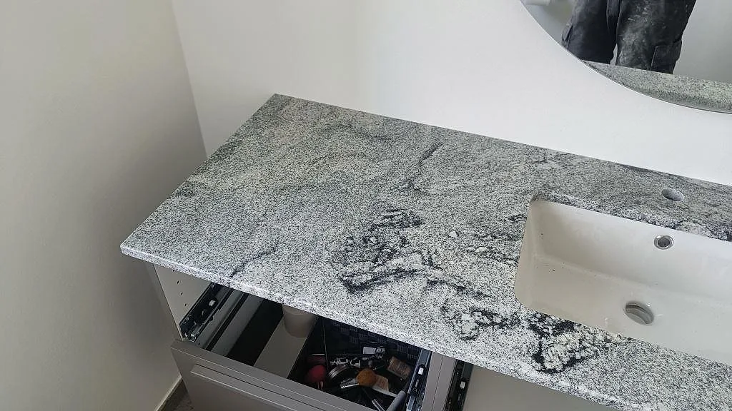 Polerad badrumsskiva i Viscont White granit med tvättställ, spegelreflektion och mörka naturstensmönster i Ringsted.
