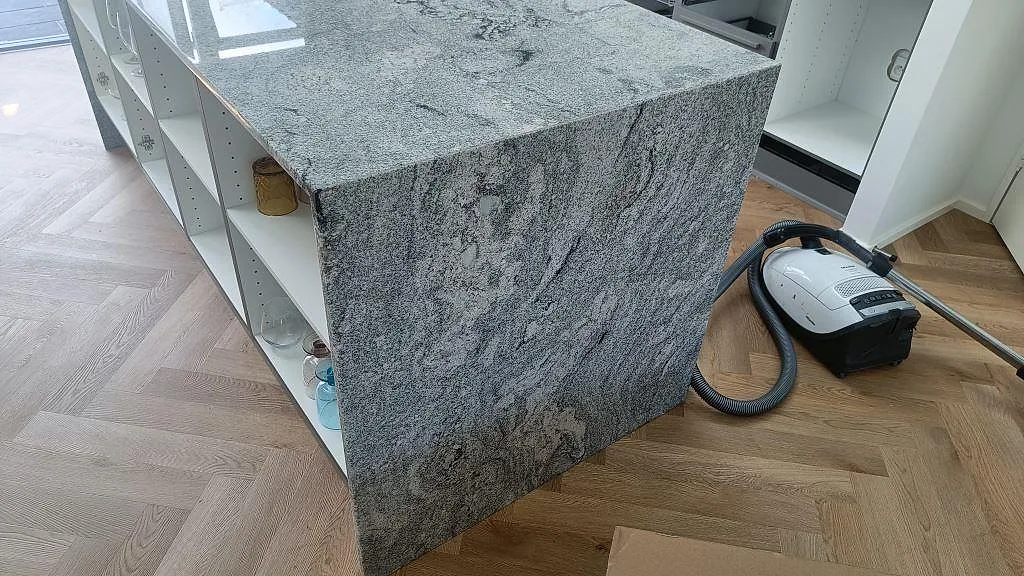 Köksö i Viscont White granit med neddragen sidoyta, polerad yta och fiskbensgolv under montering i Ringsted.