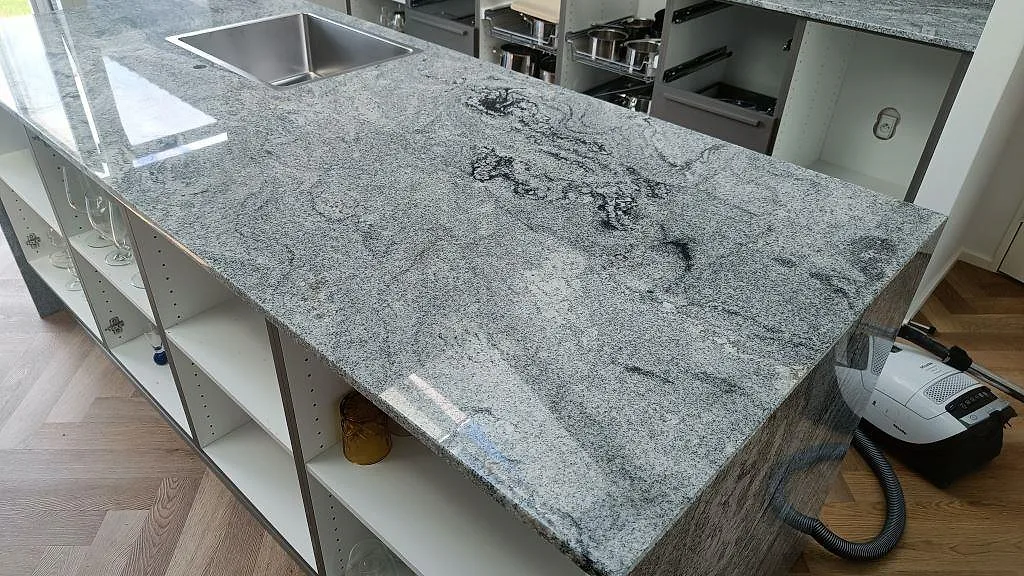 Polerad köksö i Viscont White granit med rostfri diskho, grå ådring och öppen skåpsmontering i Ringsted.