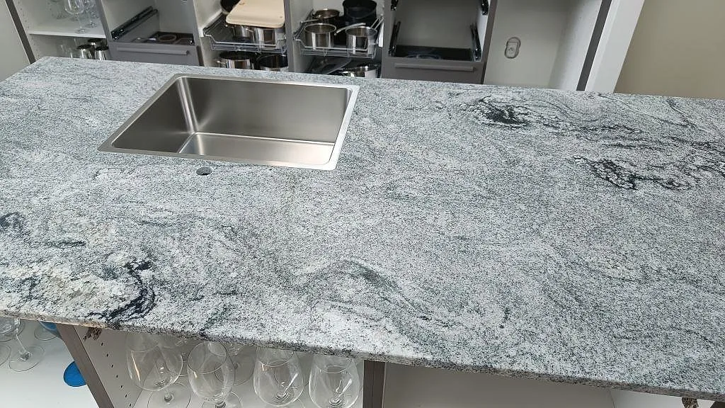 Närbild av 20 mm polerad Viscont White granit på köksö med rostfri diskho och mörka ådringar i Ringsted.
