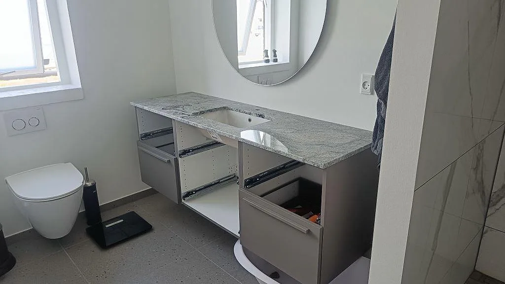 Badrumsskiva i polerad Viscont White granit med tvättställ, spegel och vit kommod under montering i Ringsted.
