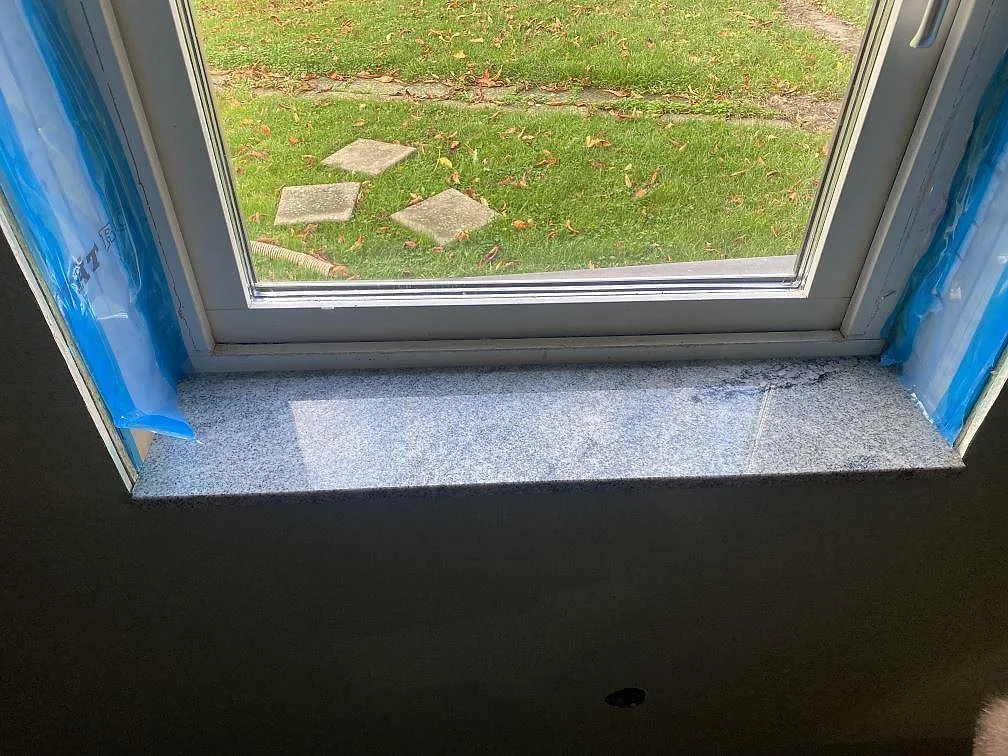 Närbild på polerad fönsterbänk i Viscont White granit med ljusgrå yta och mörk ådring i Skurup.