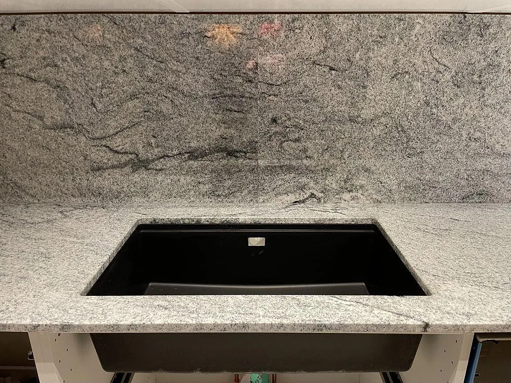 Underlimmad svart diskho infälld i polerad Viscont White granitbänkskiva med grå ådring i ett kök i Sollentuna.