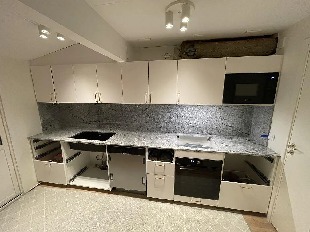 Köksbänkskiva i granit Viscont White, polerad, med heltäckande granitstänkvägg och underlimmad svart diskho i ett kök under montering i Sollentuna.