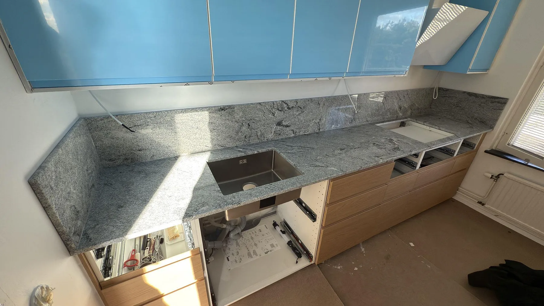 Köksbänkskiva i polerad Viscont White granit med uppvikt stänkkant i ett kök under montering i Solna.