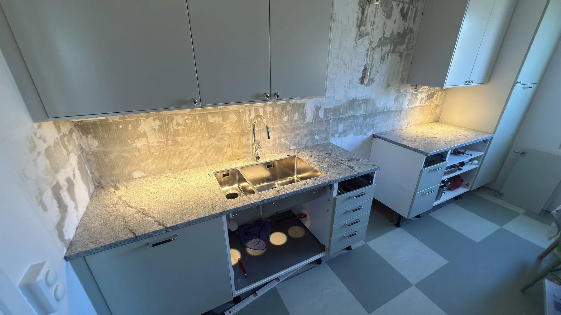 Vinkelställd köksbänkskiva i Viscont White, vit granit med grå och svarta ådror och polerad yta, med underlimmad rostfri diskho och stänkskydd i samma sten, fotograferad under montering i ett kök i Solna.